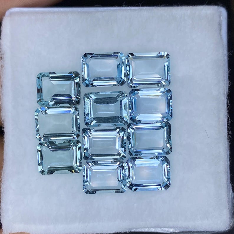 Puede incluir: Una colecci&oacute;n de 12 piedras preciosas de aguamarina azul claro en talla esmeralda rectangular. Las piedras preciosas est&aacute;n dispuestas en una caja con forro blanco.