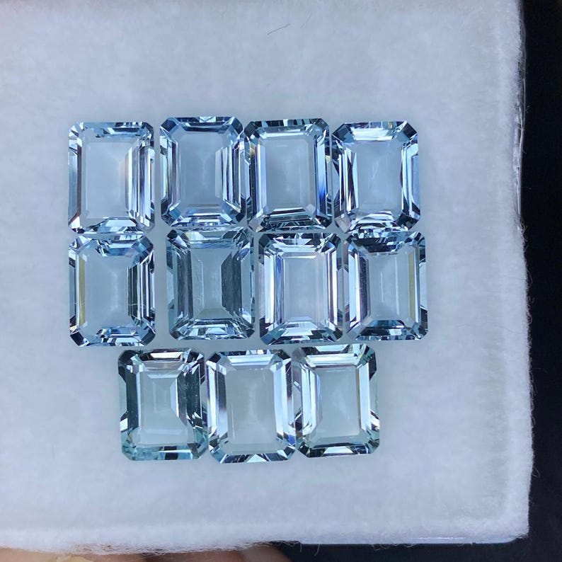 Puede incluir: Una colecci&oacute;n de 12 piedras preciosas de aguamarina azul claro, talladas en forma de esmeralda. Las piedras preciosas est&aacute;n dispuestas en tres filas de cuatro, con la fila inferior ligeramente desplazada.