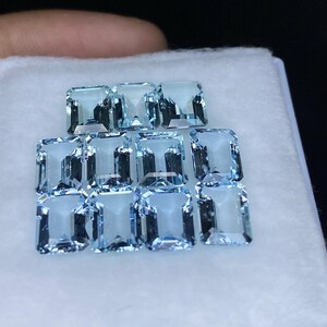 Puede incluir: Una colecci&oacute;n de piedras preciosas de aguamarina azul claro, talladas en forma de esmeralda. Las piedras preciosas est&aacute;n dispuestas en filas, con las piedras m&aacute;s grandes en la parte delantera y las m&aacute;s peque&ntilde;as en la parte trasera.