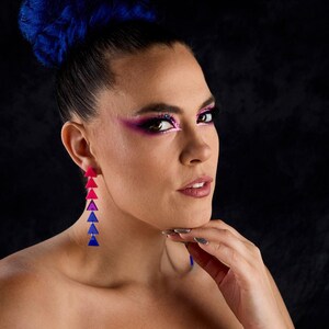 Peut inclure: Longues boucles d'oreilles pendantes composées de triangles roses, violets et bleus. La femme porte un maquillage assorti et des cheveux bleus. Le fond est sombre et fumé. Un accessoire de mode audacieux et coloré.