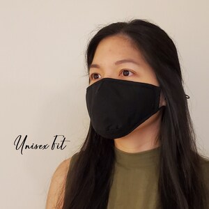 May include: A black face mask with ear loops is worn by a person. The mask covers the nose and mouth. The text "Unisex Fit" is written in cursive on the left side of the image. The person is wearing a green top.