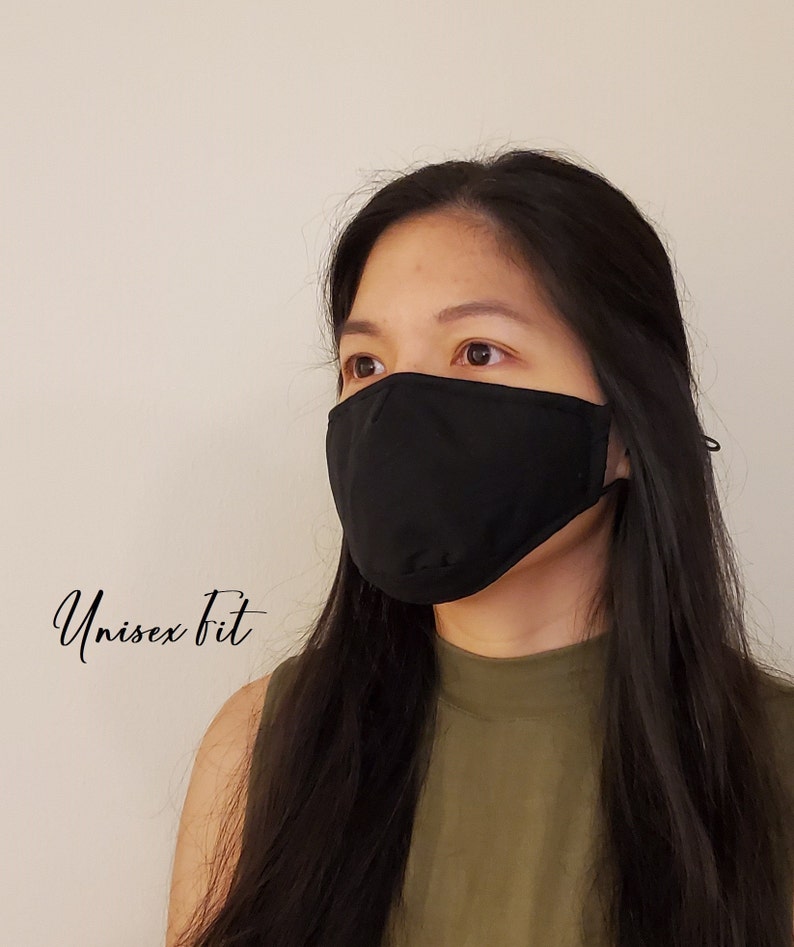 May include: A black face mask with ear loops is worn by a person. The mask covers the nose and mouth. The text "Unisex Fit" is written in cursive on the left side of the image. The person is wearing a green top.