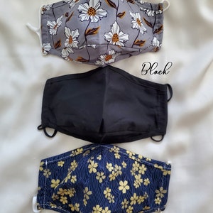 May include: Three face masks in different patterns. The top mask is grey with white floral print, the middle mask is solid black, and the bottom mask is navy blue with gold floral print. The text "Grey Floral", "Black", and "Denim Sakura" are written on the image.