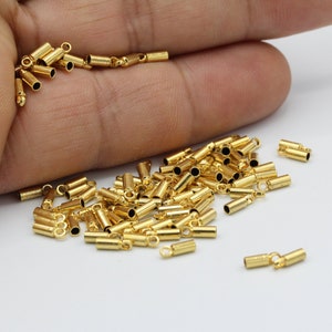 May include: A pile of gold-coloured metal end caps for jewellery making. The end caps have a small loop on one end and are cylindrical in shape.