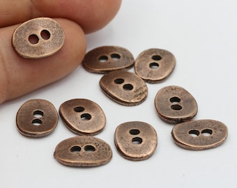 May include: A group of ten oval-shaped copper buttons with two holes each. The buttons are scattered on a white surface.
