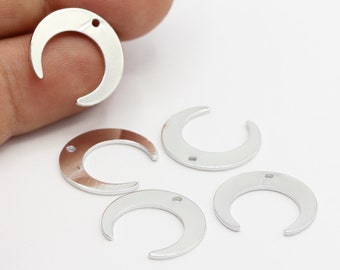 May include: Five silver crescent moon charms with a hole at the top and a smaller hole on the side. The charms are about 1 inch in diameter.