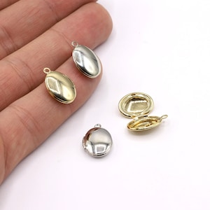 Op de afbeelding: Vier ovale medaillon hangers, twee goud en twee zilver, met een scharnierende opening. De hangers worden getoond op een wit oppervlak.