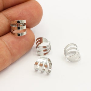 May include: Four silver ear cuffs with a simple, geometric design. Each cuff has three horizontal bands with cutouts.