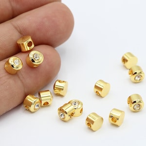 Może przedstawiać: Zbiór złotych metalowych koralików z przezroczystymi kryształkami. Korale mają otwór w środku do nawlekania.