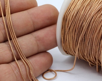 May include: A spool of gold-colored elastic cord, with a close-up of the cord in a hand. The cord is smooth and has a slight sheen.