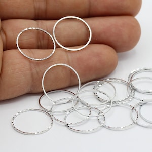 Puede incluir: Un grupo de anillos de metal plateados con una superficie texturizada. Los anillos están dispuestos en una pila sobre una superficie blanca.