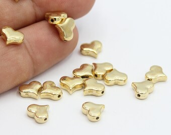 May include: A collection of gold-colored heart-shaped metal beads. The beads have a hole in the center for stringing.