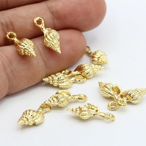 Puede incluir: Una colección de abalorios de concha de mar de metal dorado con un bucle para sujetar a joyas u otras manualidades.