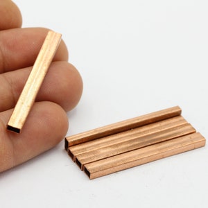May include: A close-up of a stack of five copper square tubes. The tubes are about 1 inch long and have a smooth, polished finish.