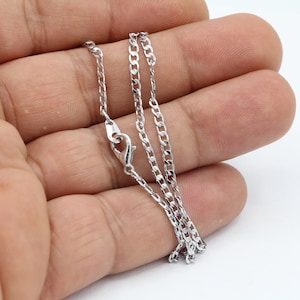 Könnte beinhalten: Eine silberne Curb-Kette mit einem Karabinerverschluss.