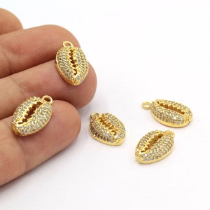 May include: Four gold-tone cowrie shell charms with clear rhinestone accents. The charms have a loop at the top for attaching to jewelry.