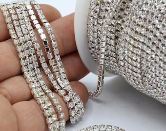Könnte beinhalten: Eine Rolle silberne Strass-Kettenborte mit klaren Strasssteinen. Die Kette besteht aus kleinen, quadratischen Strasssteinen, die durch silbernes Metall verbunden sind.