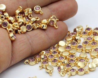 May include: A large group of gold-toned metal charms with a small, round, light purple rhinestone in the center of each charm. The charms have a loop on the top for attaching to jewelry.