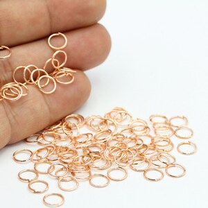 May include: A large pile of small, rose gold jump rings. The rings are about 6mm in diameter and are perfect for jewelry making.