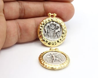 May include: Two gold-colored, round pendants with a hammered texture. Each pendant features a silver-colored coin design. One coin depicts two figures, and the other shows a single figure. The pendants have a small loop at the top for hanging.
