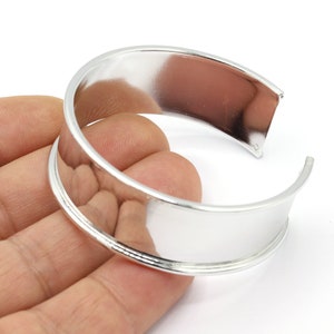 Puede incluir: Un brazalete de plata con una banda ancha y plana y un acabado liso y pulido.