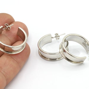 Puede incluir: Un par de pendientes de aro de plata con una banda ancha. Los pendientes son simples y elegantes.