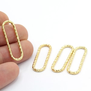 May include: Four gold-colored metal oval rings with a textured surface. The rings are approximately 1 inch in length.