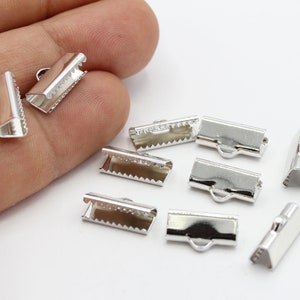 Könnte beinhalten: Silberne Metallverschlüsse zum Schmuckmachen. Die Verschlüsse sind rechteckig mit einer kleinen Schlaufe an einem Ende und einem kleinen Haken am anderen Ende. Es sind neun Verschlüsse auf dem Bild.