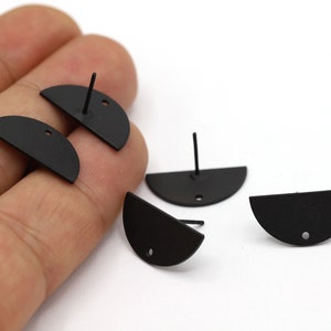 Op de afbeelding: Vier zwarte halfronde oorbel studs met een pen en een klein gaatje bovenaan. De oorbellen liggen op een wit oppervlak.