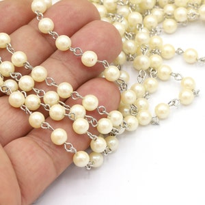May include: A strand of white pearl beads strung on a silver chain. The beads are round and smooth, and the chain is delicate.