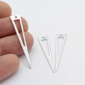 May include: Three silver triangle shaped metal charms with a hole at the top. The charms have a textured surface and a cut-out triangle in the center.