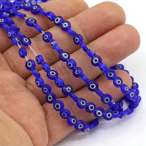 May include: A strand of blue glass beads with white evil eye designs. The beads are strung on a clear elastic cord.