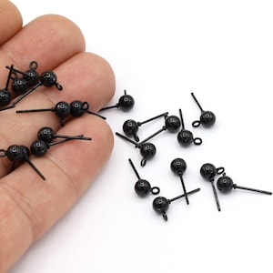 May include: A close-up of a hand holding a group of black bead earring findings. The findings have a small loop at the top and a straight pin on the bottom.