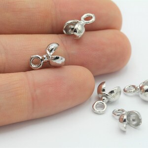May include: Silver-toned metal crimp beads with a loop on one end and a split end on the other. The beads are designed to be used for jewelry making.