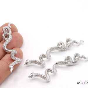 Puede incluir: Tres pendientes de plata en forma de serpiente. Cada pendiente es una serpiente enroscada con una superficie texturizada.