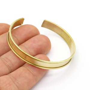 Peut inclure: Un bracelet en métal doré avec une large bande plate. Le bracelet est ouvert et présente un design simple et minimaliste.