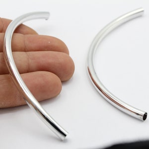 Könnte beinhalten: Zwei silberne Metallreifen, jeder mit einem Durchmesser von etwa 5 cm. Die Reifen sind gebogen und haben eine glatte, polierte Oberfläche.