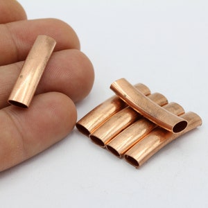 May include: A group of six copper pipe end caps, some are curved and some are straight. The caps are arranged in a stack with the curved caps on top.