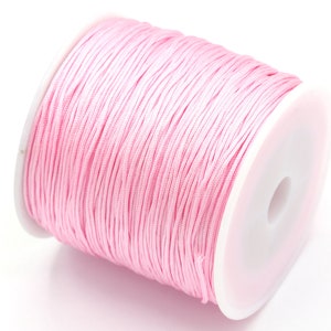 Puede incluir: Un carrete de cordón encerado rosa, un tipo de cuerda que se utiliza para la elaboración de joyas y manualidades.