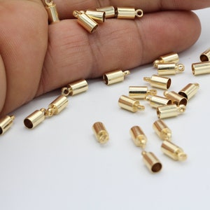 May include: A group of gold-colored metal end caps for jewelry making. The end caps are cylindrical with a small loop at the top.