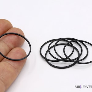 May include: A set of six black rubber rings, also known as o-rings, are shown on a white surface. One ring is being held by a hand.