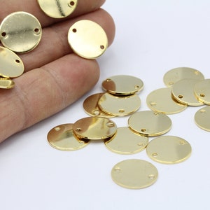 Può includere: Una collezione di cerchi in metallo dorati con due fori ciascuno. I cerchi sono sparsi su una superficie bianca.