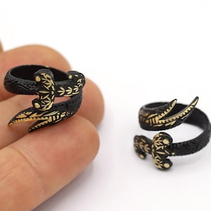 May include: Two black rings with gold detailing in the shape of a snake. The rings are on a finger and a table.