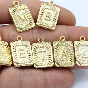 May include: Gold-toned metal charms with the letters "METAL" in a decorative font. Each charm has a loop for attaching to a necklace or bracelet.
