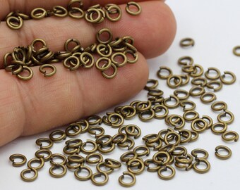 Puede incluir: Una gran cantidad de pequeños anillos de salto de color dorado. Los anillos están dispersos sobre una superficie blanca.