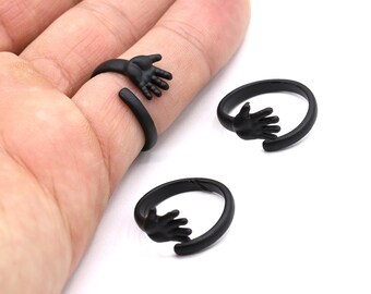 May include: Two black open rings with a hand design. The rings are made of metal and have a matte finish.