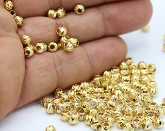 May include: A large pile of gold-colored metal beads with a textured, ribbed surface. The beads are small and round, and they are scattered on a white surface.