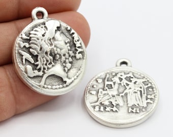 May include: Two silver-toned metal coin charms with raised designs. One charm features a profile of a woman's face with long hair. The other charm features a design of a woman holding a staff with a bird on her shoulder.
