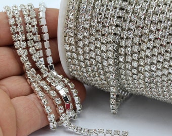 Könnte beinhalten: Eine Rolle silberne Strass-Kettenborte mit klaren Steinen. Die Kette ist in einer Hand und auf einer Spule zu sehen.