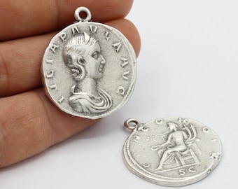 May include: Two silver-toned metal pendants in the shape of ancient Roman coins. One coin features a profile of a woman's head, the other features a seated figure.